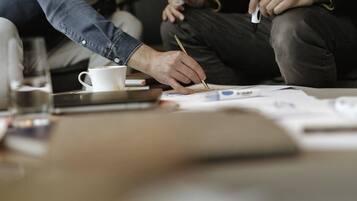 A person holding a pen, sitting at a table with papers and a cup of coffee.