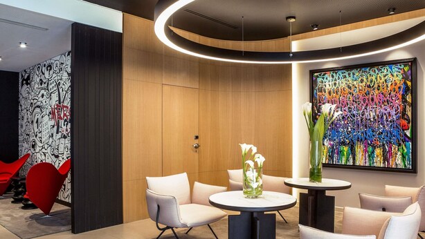 Un hall d’entrée moderne avec une table ronde, des chaises blanches et un tableau abstrait aux couleurs vives.