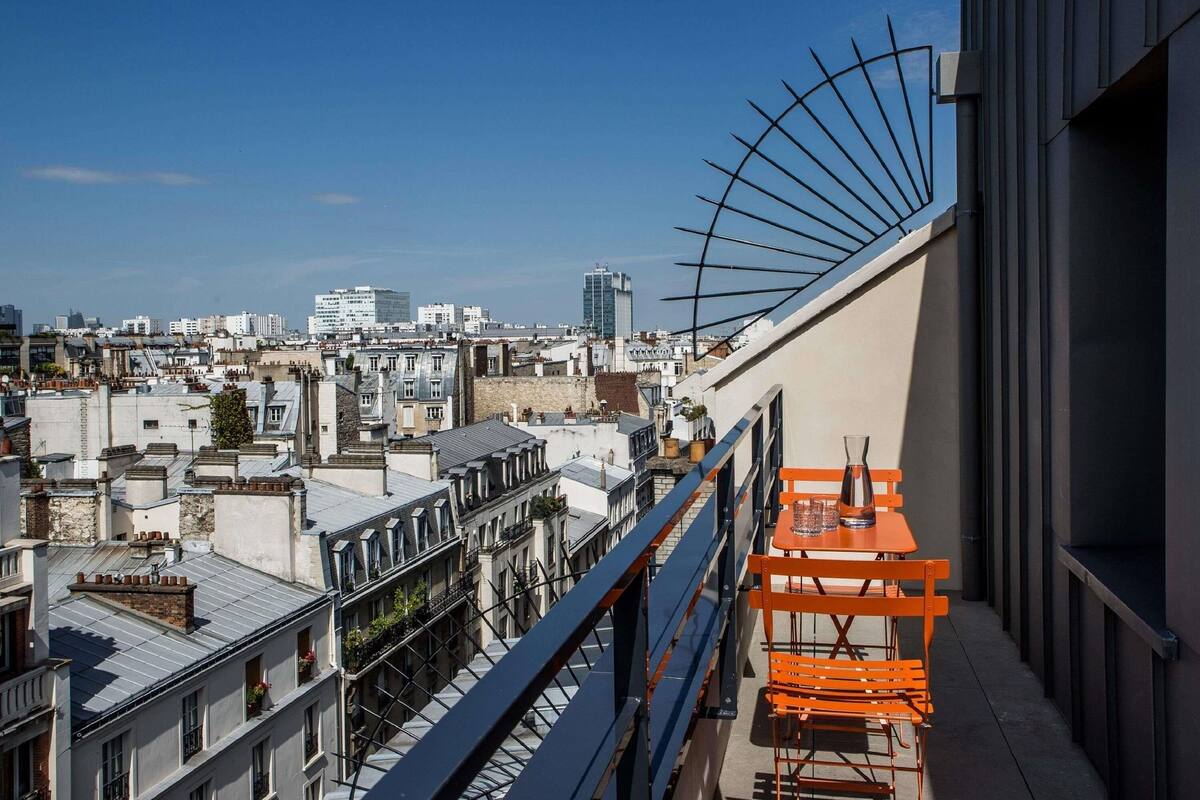 A rooftop terrace with a view of a cityscape, including buildings and a clear sky.