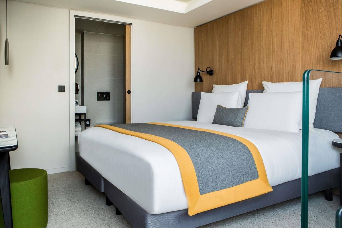 A modern hotel room with a bed, bedside table, lamp, and a wooden accent wall.