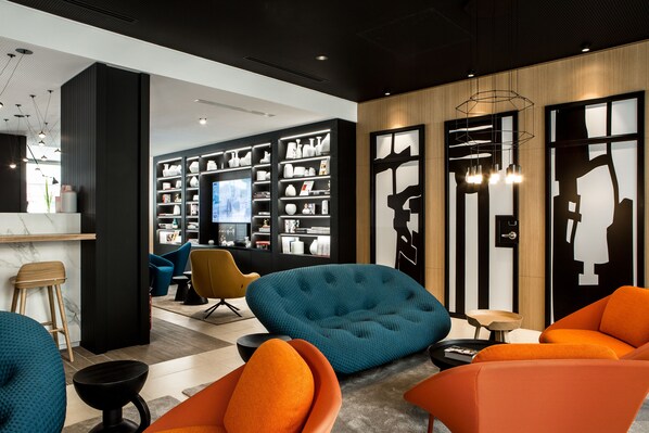 A modern interior with a seating area featuring orange and teal chairs, a television, and a wall with shelves displaying various items.