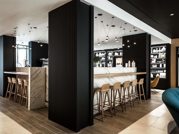 A modern bar area with marble countertops, wooden stools, and pendant lighting.