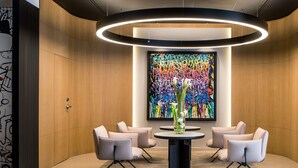Un hall d’entrée moderne avec une table ronde, quatre chaises, une peinture abstraite aux couleurs vives et un luminaire circulaire.