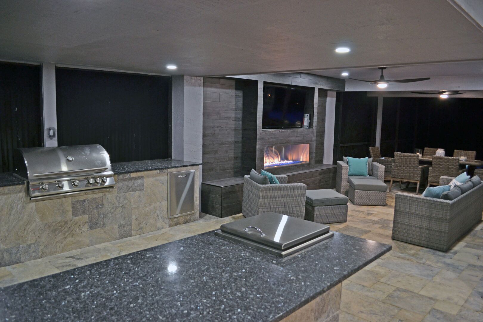 Un espace de vie extérieur doté d’une cheminée en pierre, d’un barbecue et de mobilier en osier.