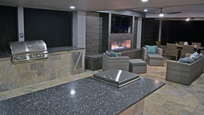 Un espacio exterior para relajarse con chimenea de piedra, una parrilla y muebles de mimbre.