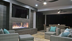 Un espacio al aire libre con chimenea, mobiliario de mimbre y ventiladores de techo.