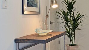 Un pasillo con una consola de madera, una lámpara de pie, una planta en maceta y un cuadro en la pared.