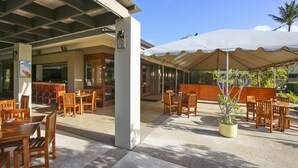 An outdoor patio area with wooden tables and chairs, a covered seating area, and a potted plant. - Turtle Bay Sea Shells. (Kahuku)