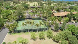 An aerial view of a residential area with a tennis court surrounded by palm trees, houses, and a view of the ocean. - Turtle Bay Sea Shells. (Kahuku)