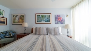 A hotel room with a large bed, two bedside tables with lamps, a chair, and three framed artworks on the wall. - Turtle Bay Sea Shells. (Kahuku)
