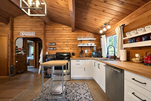 A wooden interior with a kitchen area featuring a stove, microwave, and shelves with dishes. - Near Lake Wenatchee|Fence|Hot Tub|WIFI|Dogs|Sleep4 (Leavenworth)