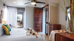 Une chambre à coucher avec un lit, une armoire en bois, un ventilateur de plafond et une vue sur l’extérieur.