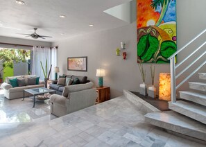 A spacious living room with a sofa set, a coffee table, and a staircase leading to an upper level.