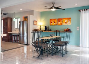 A modern kitchen with a dining area, featuring a glass-top table, metal chairs, and a ceiling fan.