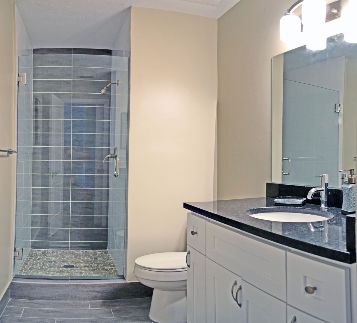 A modern bathroom with a glass shower enclosure, a white toilet, and a black countertop with a sink.