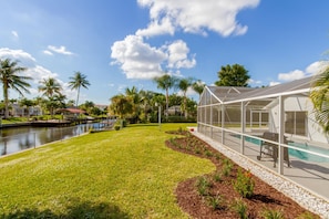 A poolside area with a covered seating area, a water canal, and lush greenery.