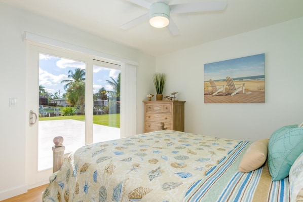 A bedroom with a bed, a dresser, a painting, and a view of the outdoors.
