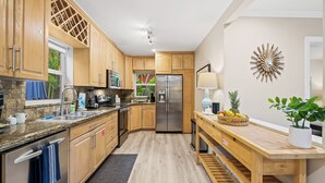 A modern kitchen with wooden cabinets, stainless steel appliances, a granite countertop, and a central island with a lamp and fruit bowl. - Private Tropical Escape Near Fort Lauderdale Beaches & Dining! (Fort Lauderdale)