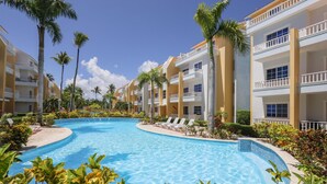 A resort with a swimming pool, palm trees, and multiple-story buildings with balconies. - Estrella Del Mar H6_200Mbps_BBQ_Pool_Walk to Beach (Bavaro-Punta Cana)