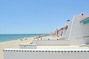 Un hôtel situé en bord de mer, avec une façade blanche, une terrasse carrelée et une vue sur l’océan.