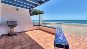 Une terrasse avec un barbecue, des sièges d’extérieur et une vue sur la plage.