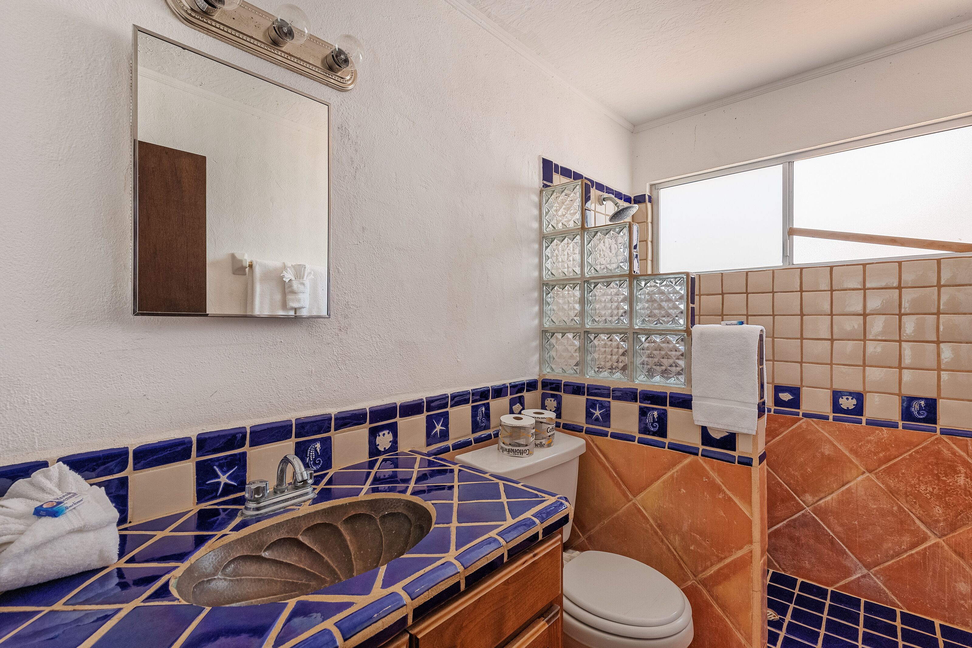 Une salle de bain équipée d’un lavabo, d’un miroir, de toilettes et d’une fenêtre donnant sur un paysage agréable.