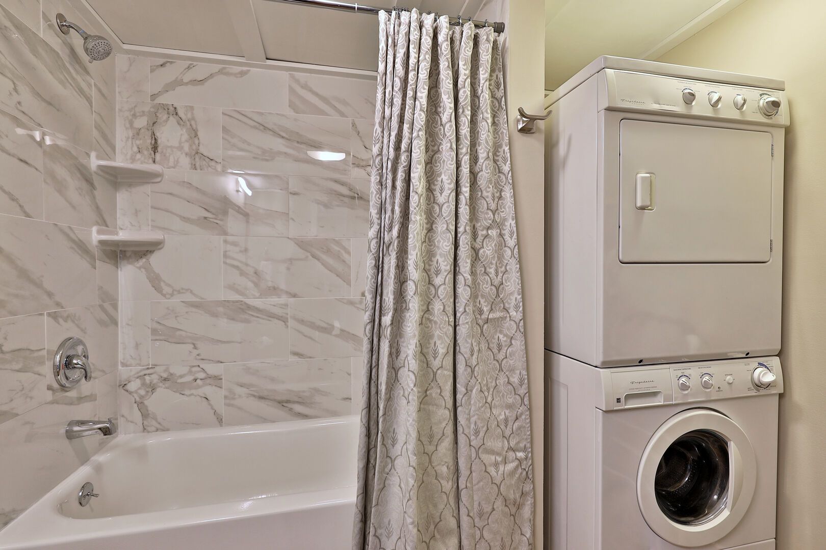 Un bagno con doccia in marmo, una vasca da bagno, una lavatrice e un'asciugatrice.