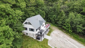 Et hus med saddeltag, en balkon med udendørs møbler, og en grusindkørsel.