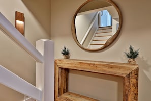 A wooden console table with a mirror above it, reflecting a staircase.