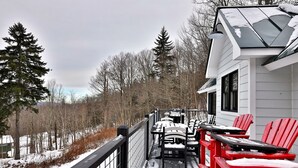 En overdækket terrasse med røde Adirondack-stole og et bord, omgivet af sneklædte træer og en hvid bygning.