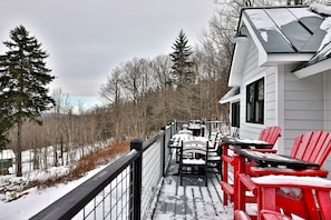 A snow-covered deck with outdoor seating and a view of a forested area.