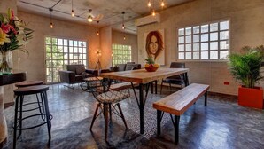 A spacious room with a large table, bar stools, and a bench. There are large windows with a view of greenery outside. - Comfortable apartment only 3 blocks from 5th av (Playa del carmen)