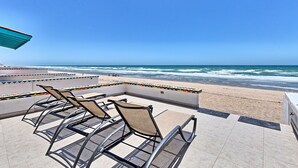 Een terras aan het strand met ligbedden en uitzicht op de oceaan.