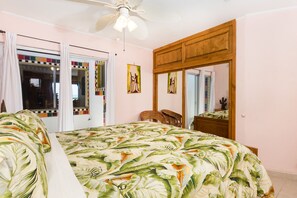 A bedroom with a bed, a ceiling fan, a wooden wardrobe, and a mirror.