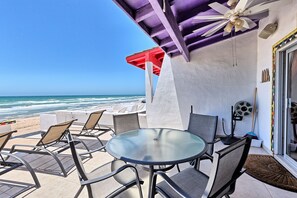 A patio with a glass table and chairs, a red umbrella, and a view of the ocean.