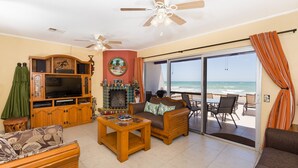 Een woonkamer met een televisie, houten meubels, een open haard en uitzicht op de oceaan.