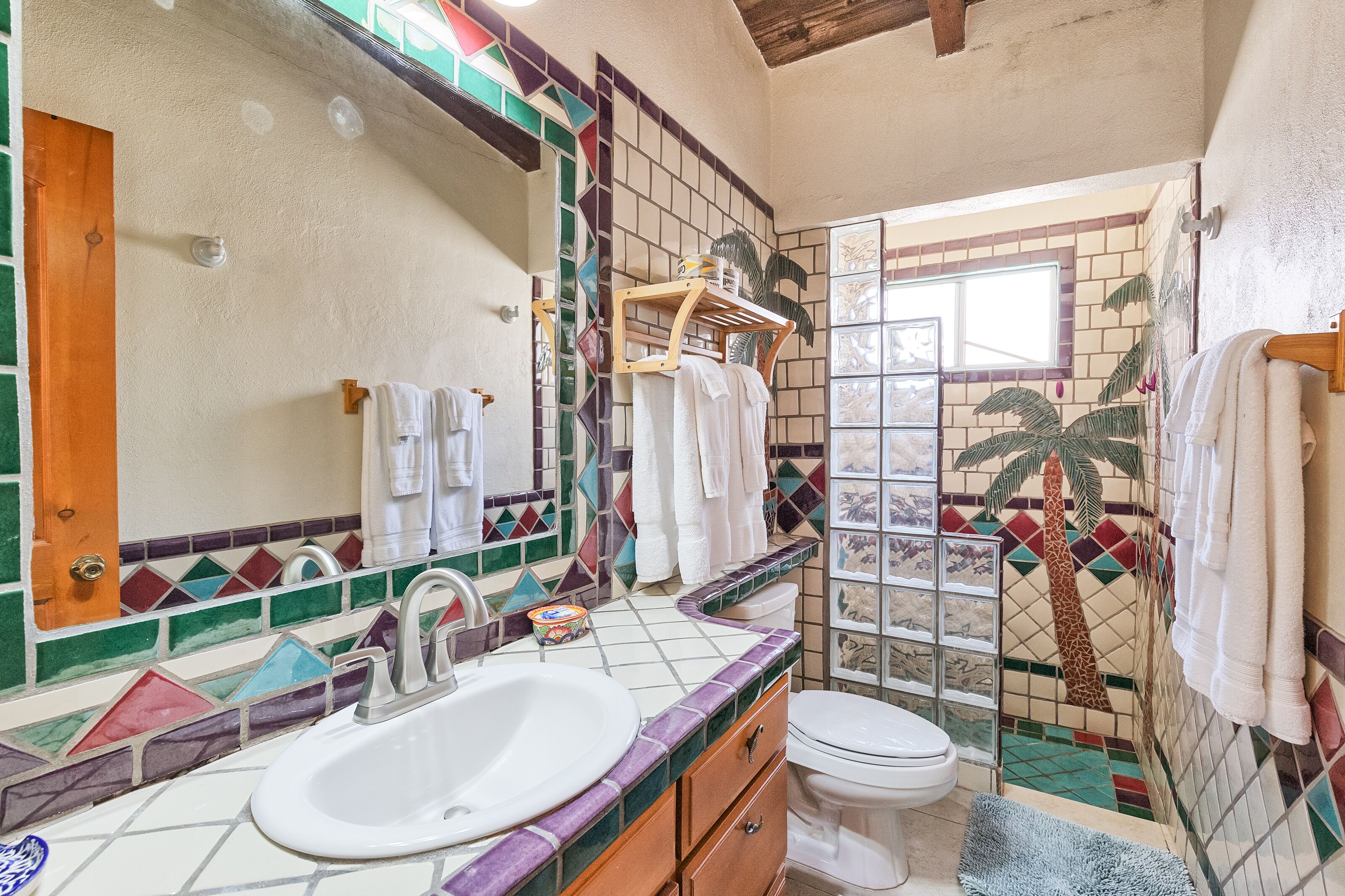 Een badkamer met een wastafel, toilet en een douchegedeelte met een betegelde wand met een ontwerp van een palmboom.