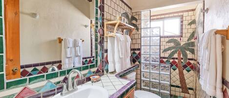 Een badkamer met een wastafel, toilet en een douchegedeelte met een betegelde wand met een ontwerp van een palmboom.
