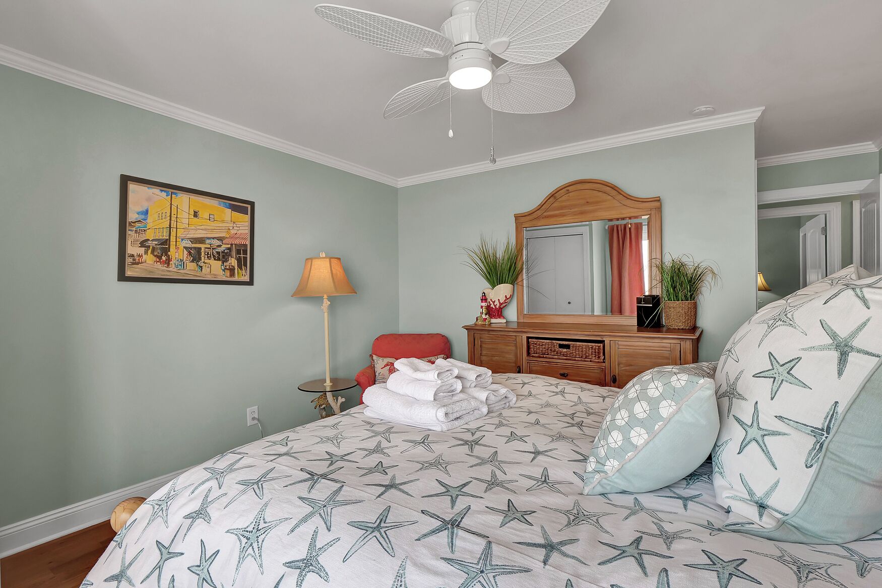 A bedroom with a bed, a dresser, a mirror, a lamp, and a painting on the wall.