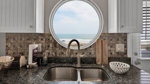 Eine Küche mit einem großen Fenster zum Strand, einem doppelten Waschbecken und einer Seifenspender.