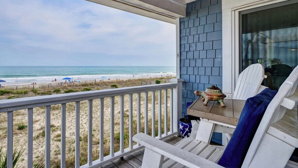 Ein Balkon mit Blick auf den Strand, ein weißer Stuhl und ein kleiner Tisch mit einer Dekoration.