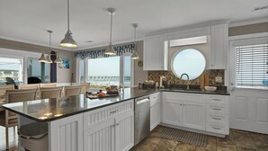 Eine moderne Küche mit weißen Schränken, einer großen Kochinsel und Blick auf den Strand.