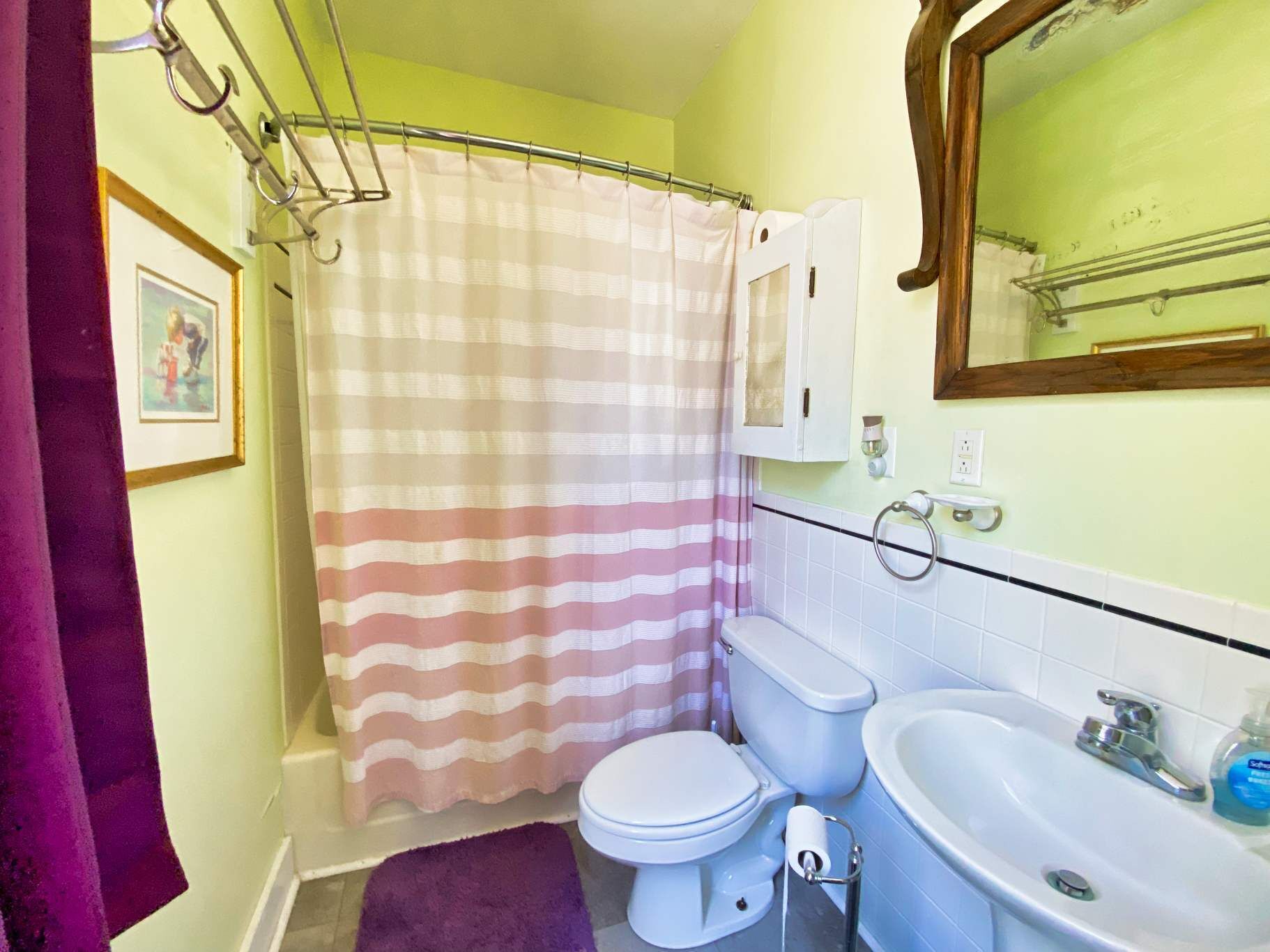 A bathroom with a striped shower curtain, a toilet, a sink, and a mirror.