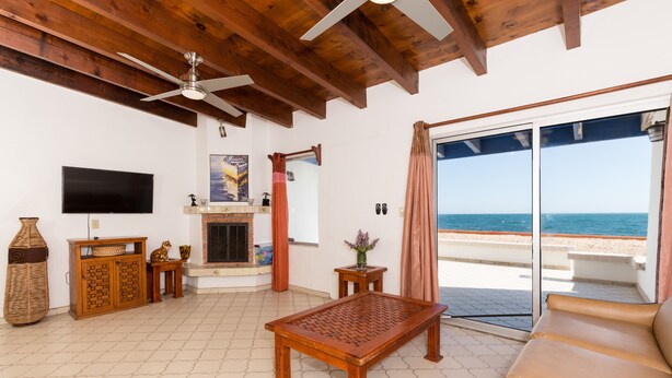 Un salon avec un plafond en bois, un téléviseur, une cheminée et une vue sur la mer.