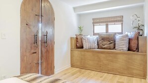 Een kamer met een houten bank, een grote houten deur en een raam met zonwering.