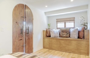 A room with a wooden bench, a large wooden door, and a window with blinds.