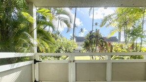 A covered outdoor seating area with a view of tropical vegetation and a building in the background. - Plantation Hale Suites G5, King Bed, AC, Near Ocean, Shops & Restaurants (Kapaa)