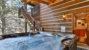 A hot tub with a wooden deck and stairs leading to a wooden cabin.