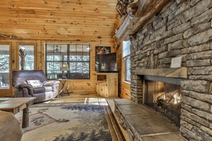 A log cabin interior with a stone fireplace, wooden walls, a leather sofa, and a television. - PICK'S RIVERSIDE RETREAT - 2 Bedroom plus Loft Riverside Retreat on the Upper Toccoa River (Blue Ridge)