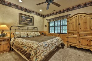 Une chambre à coucher avec un lit, une armoire en bois, un tableau, une fenêtre avec des rideaux et un ventilateur de plafond.